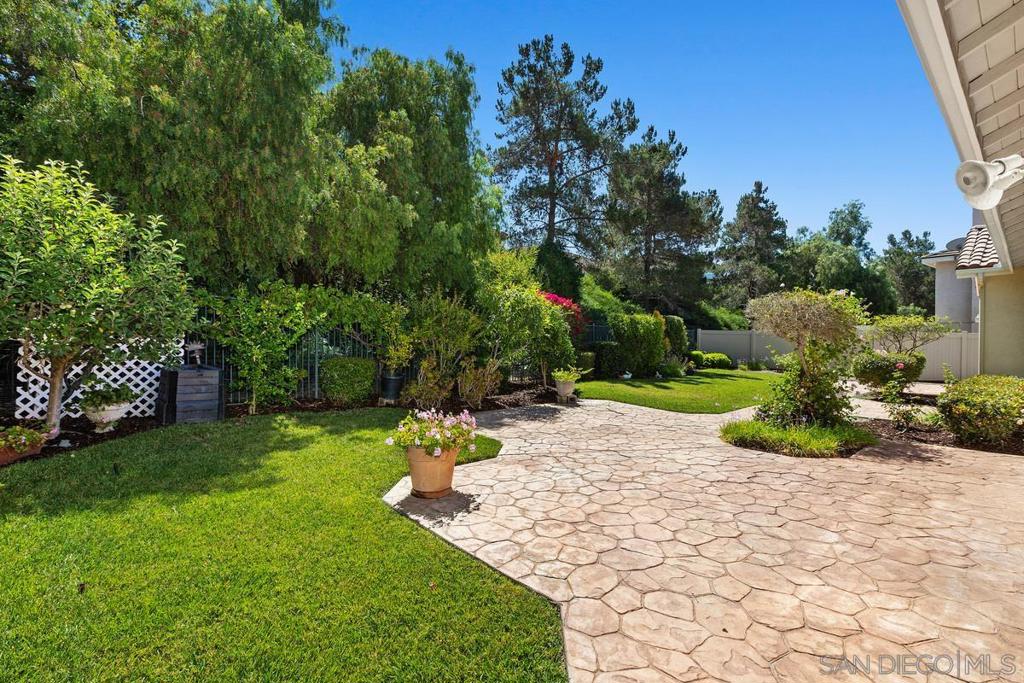 Backyard patio with stone paving, lawn, mature trees, and flowering shrubs.