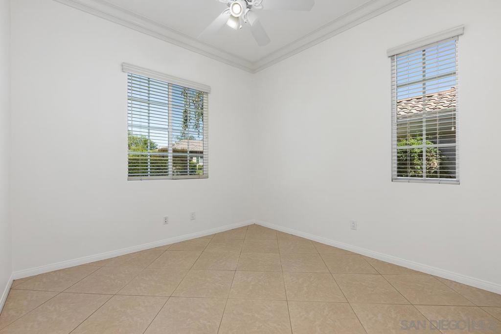 Empty tiled room with two windows and a ceiling fan.