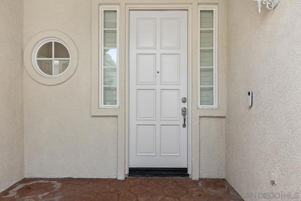 Front entry with a white paneled door, round window, narrow sidelights, and stone-paved porch.