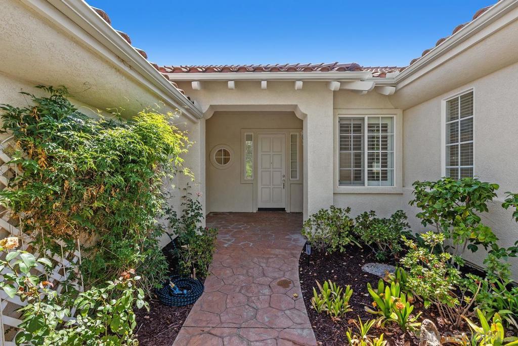Home’s front entry with a red-tile walkway, stucco walls, and landscaped garden beds.