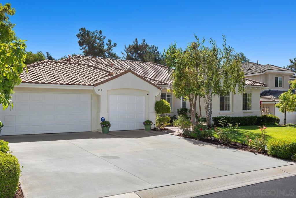 Stucco home with a tile roof, wide driveway, and landscaped front yard.