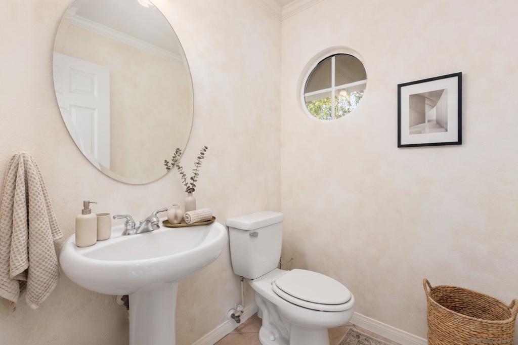 Powder room with a pedestal sink, oval mirror, and round window above the toilet.