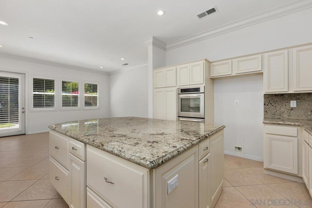 Kitchen with a large granite island, white cabinetry, and a built-in oven.
