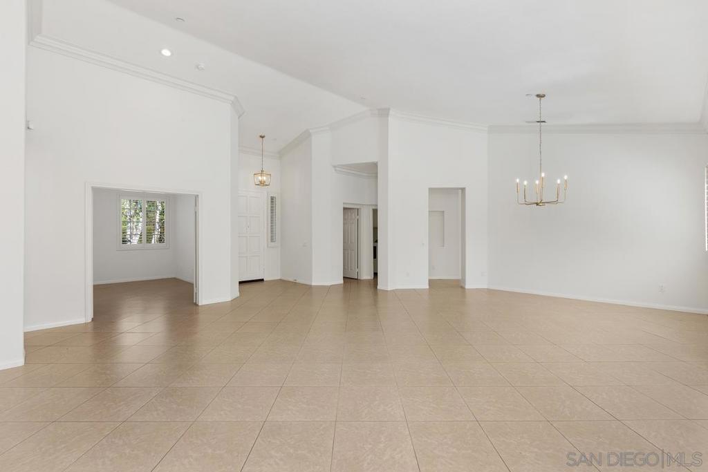 Empty spacious room with beige tile floors, high ceilings, and a chandelier.