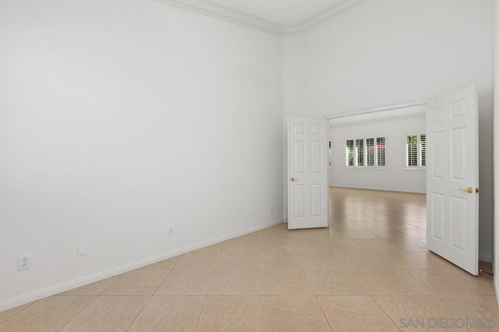 Empty tiled room with white double doors opening to a bright adjoining room.