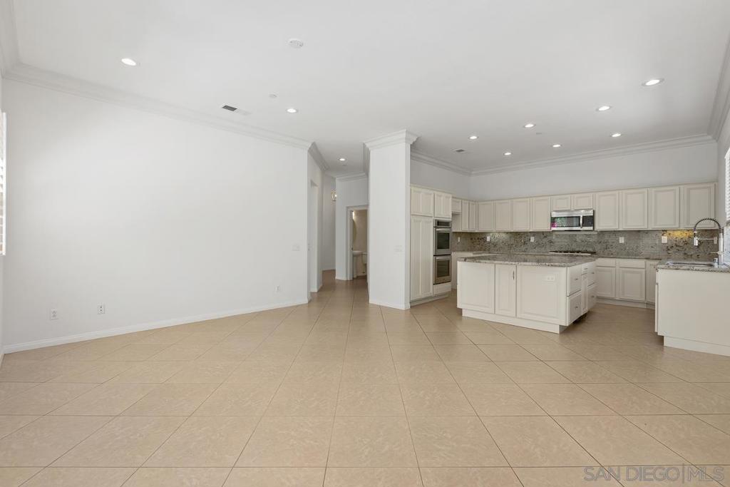 Open-plan kitchen with white cabinetry, a large island, stone counters, and beige tile flooring.