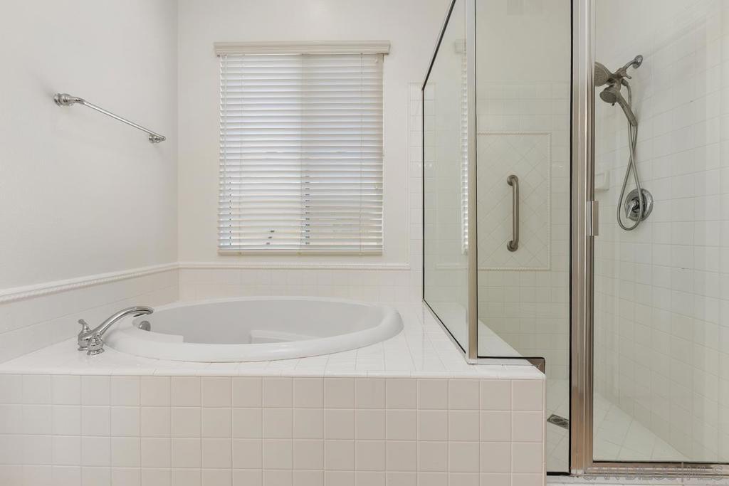 Bathroom with a built-in soaking tub and glass-enclosed tiled shower beside a window with white blinds.