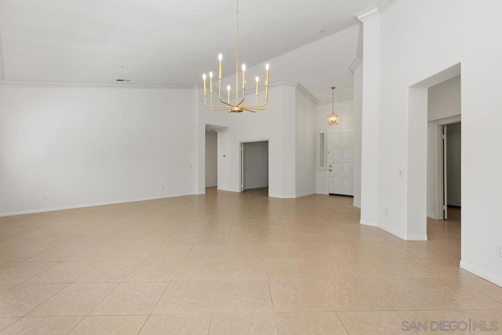 Vacant open living area with beige tile floors and a brass chandelier.