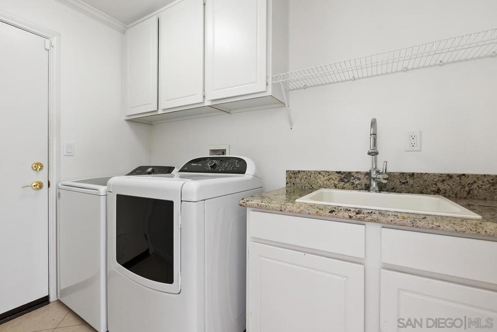 Laundry room with a white washer and dryer beside a granite countertop and utility sink.