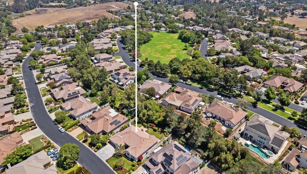 Aerial neighborhood view with a white marker pointing to a tan-roofed house near a green field.