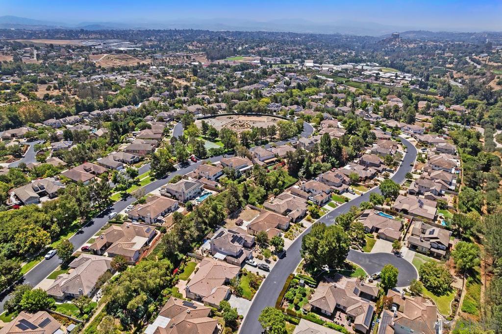 Aerial view of homes along winding streets, with a landscaped circular park and distant hills.