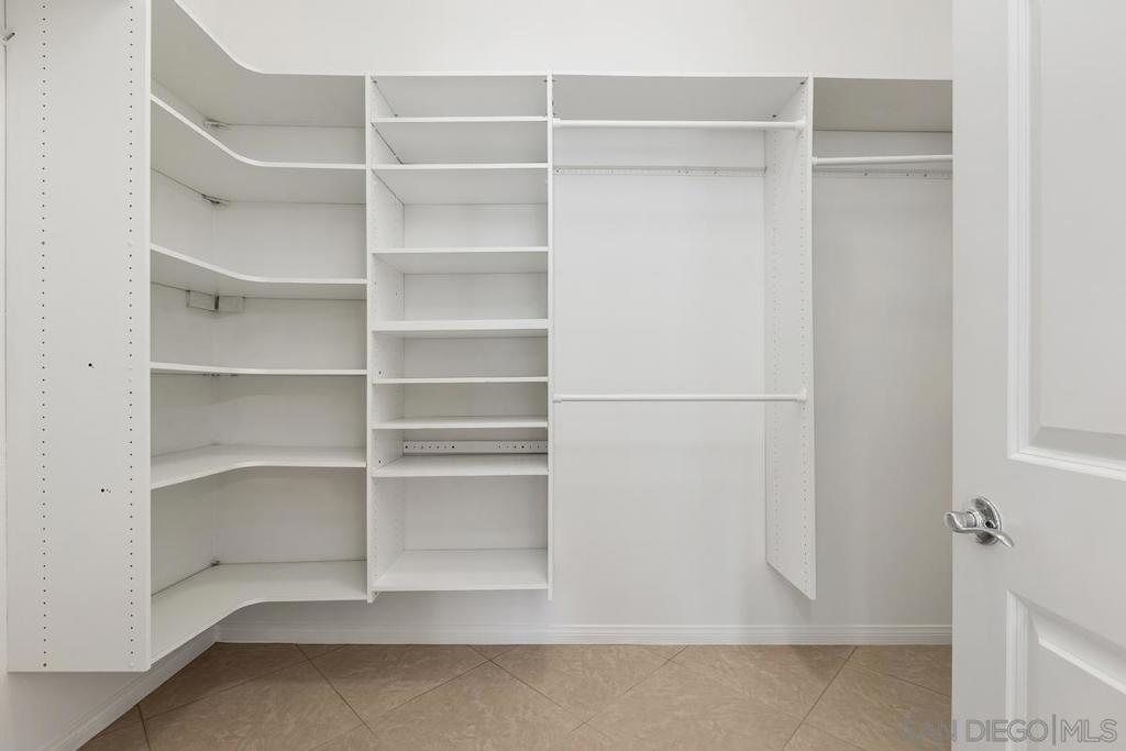 Walk-in closet with white built-in shelving and beige tile flooring.