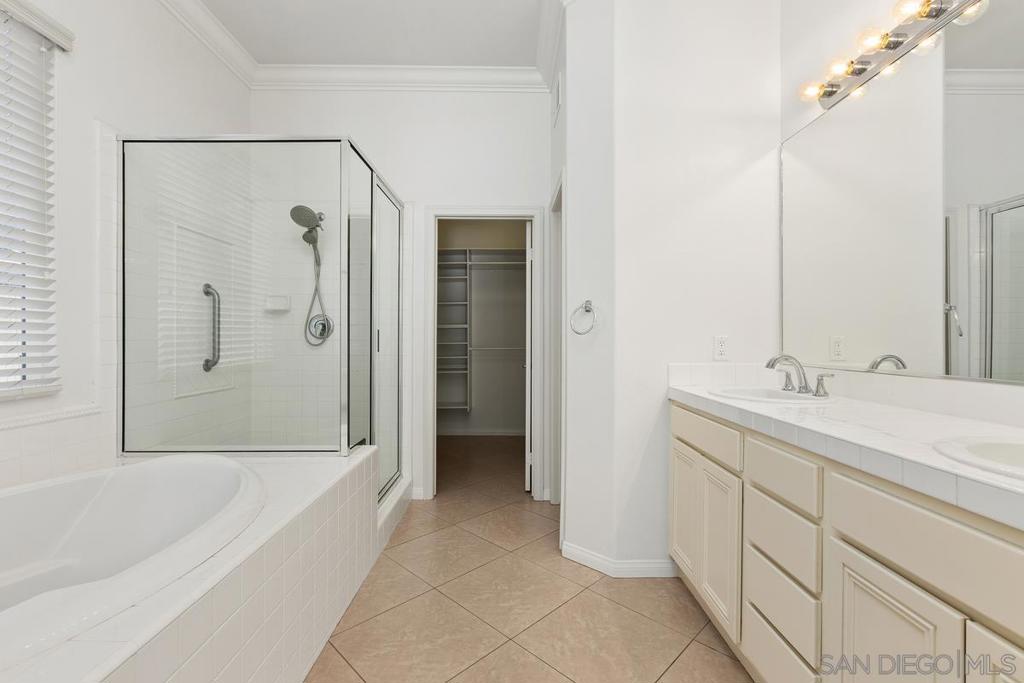 Bathroom with a soaking tub, glass shower, dual-sink vanity, and open walk-in closet.