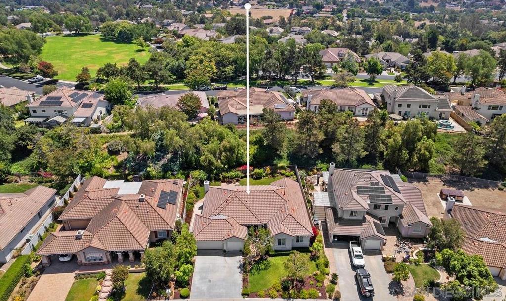 Aerial view of a tile-roofed home marked by a white locator line, with a green open space beyond the neighborhood.