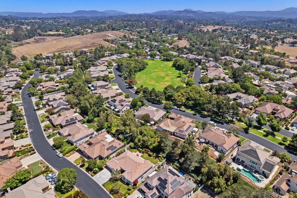 Aerial view of suburban homes around a grassy open space, with hills in the distance.