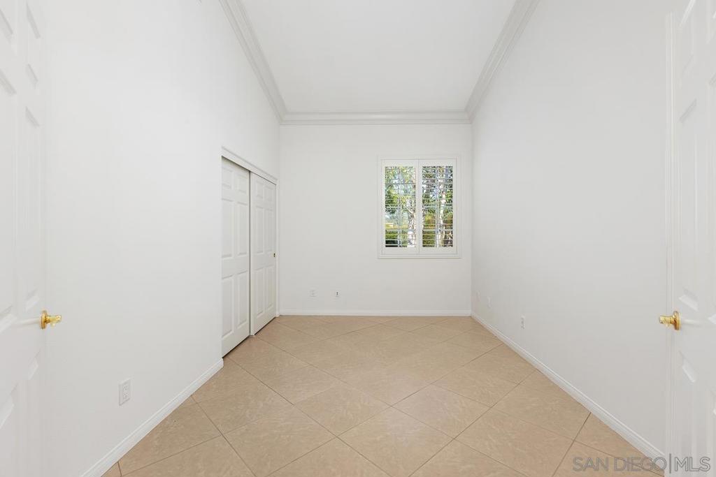 Empty room with beige tile flooring, sliding closet doors, and a shuttered window.