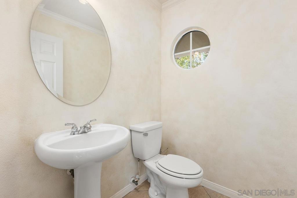 Bathroom with a pedestal sink, toilet, large oval mirror, and round window.