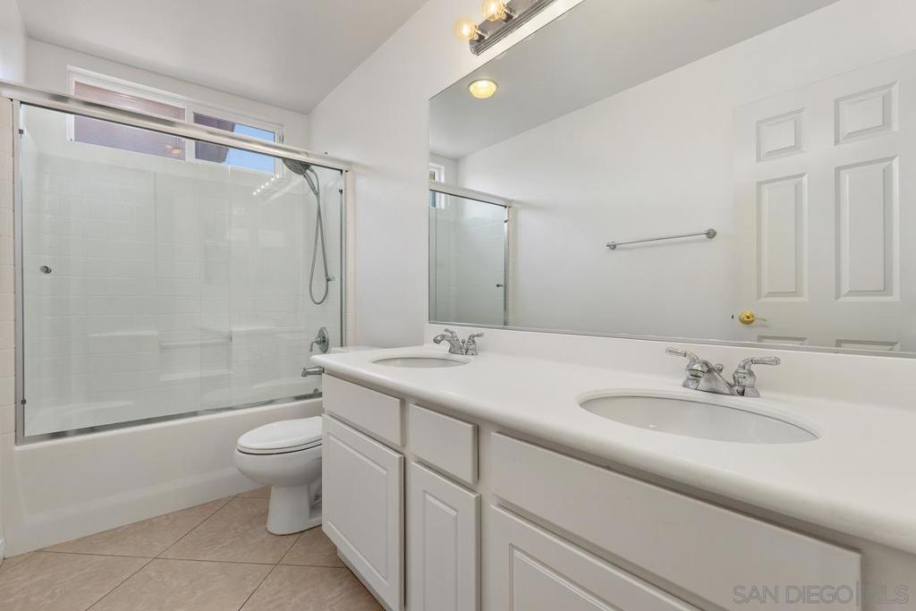 Bathroom with a double-sink vanity and glass-enclosed tub and shower.