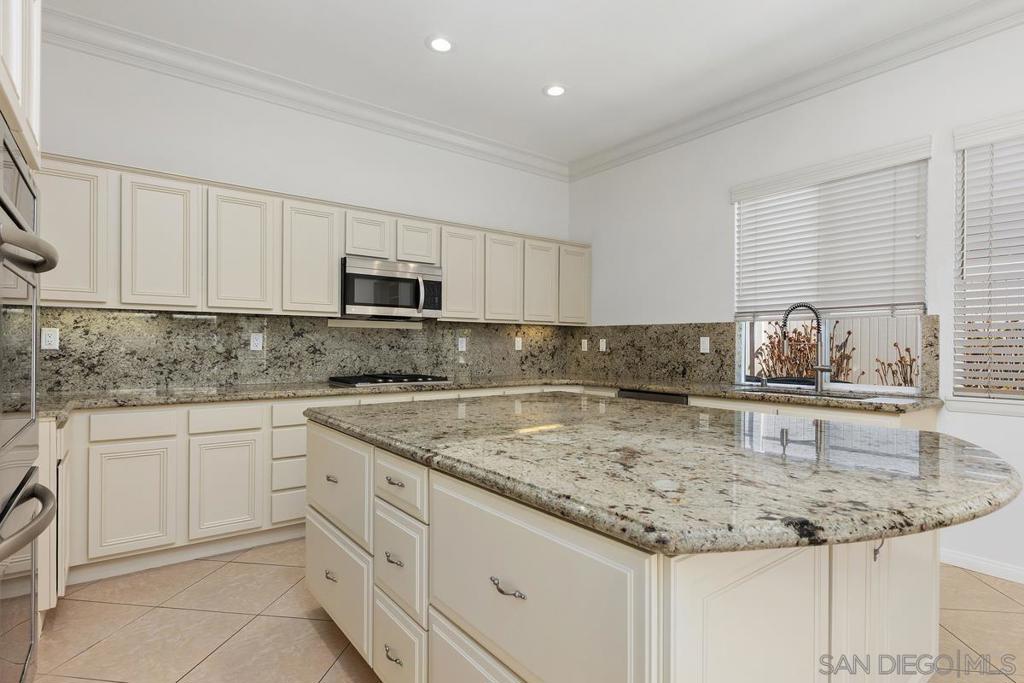 Kitchen with a large granite island, cream cabinetry, and a window above the sink.