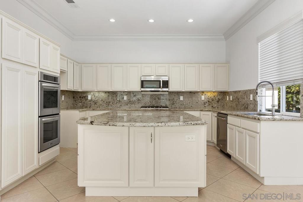 Bright kitchen with white cabinets, granite counters, a large island, and double wall ovens.