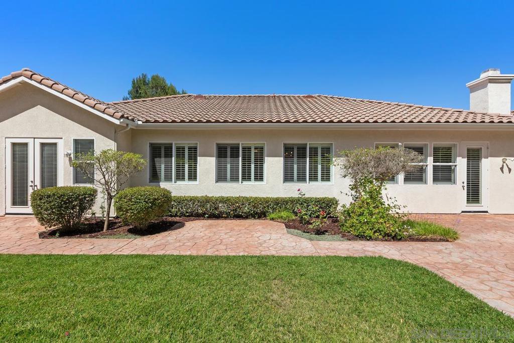 Rear of a single-story stucco home with a curved patio, trimmed shrubs, and green lawn.