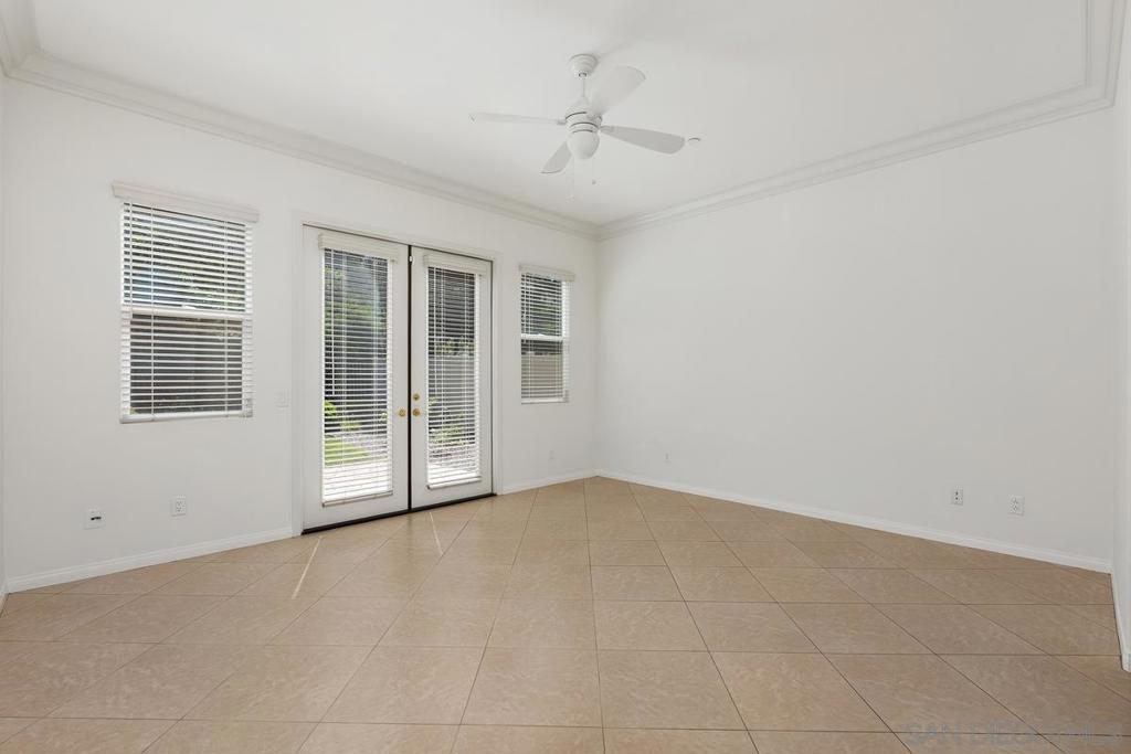 Empty tiled room with a ceiling fan and double doors opening to the outdoors.