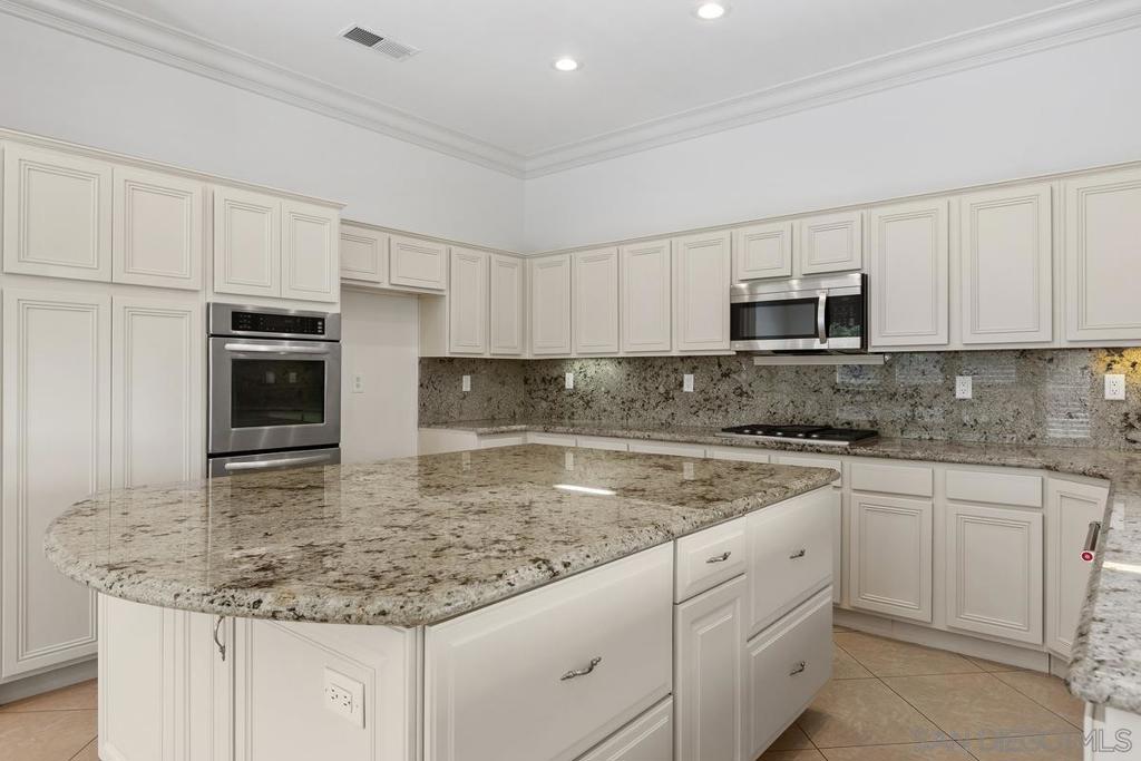 Kitchen with white cabinetry, granite counters, a large island, and stainless-steel appliances.