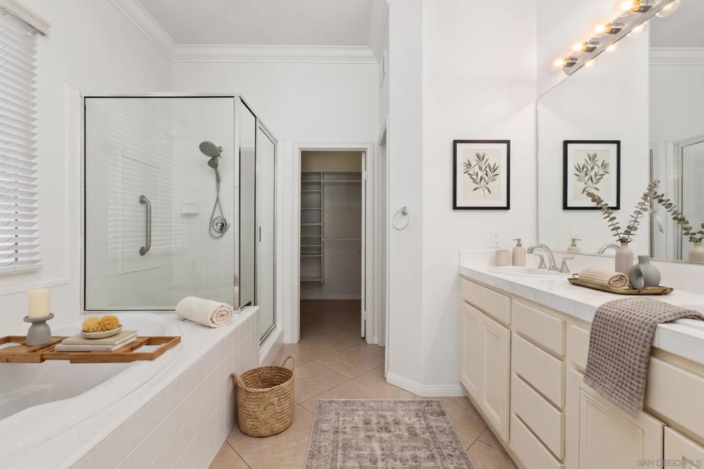 Bathroom with a glass shower, large bathtub, cream double vanity, and doorway to a walk-in closet.