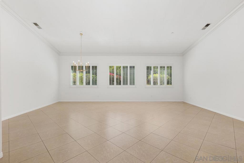 Empty room with beige tile floors, three shuttered windows, and a hanging chandelier.