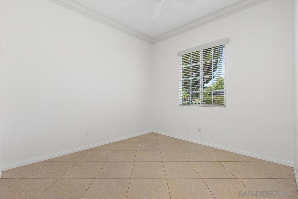 Empty room with beige tile flooring, white walls, and a window with blinds.