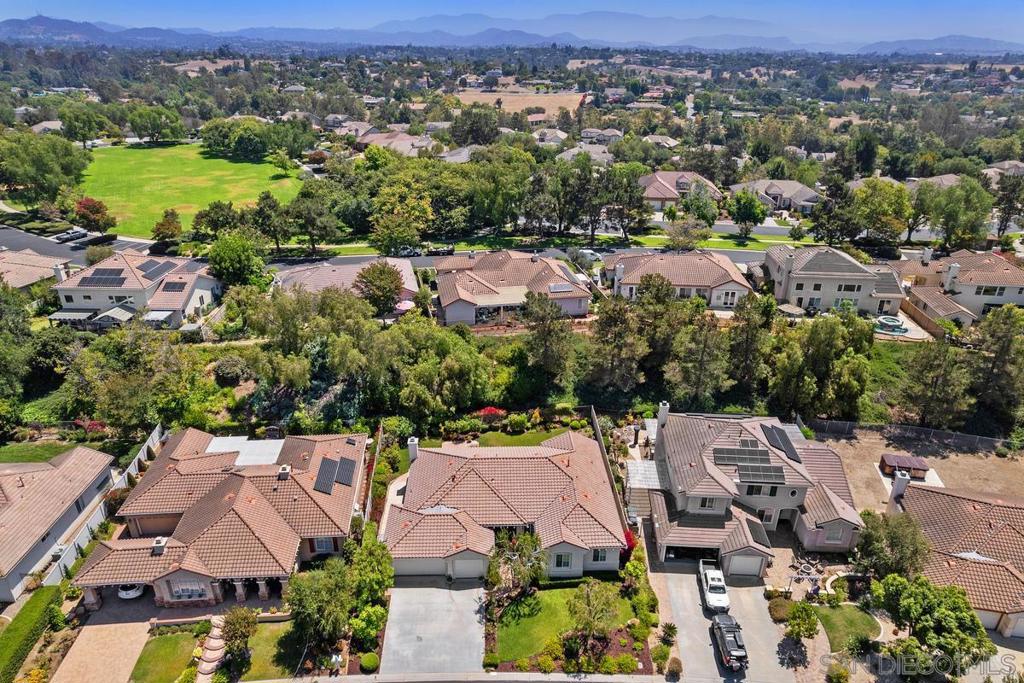 Aerial view of homes, a green open space, and distant mountain ranges.