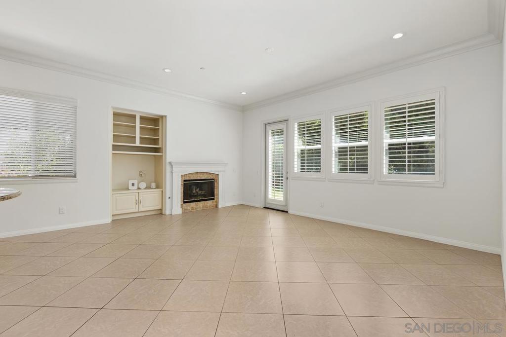 Empty living room with tiled floors, built-in shelving, a fireplace, and shuttered windows.