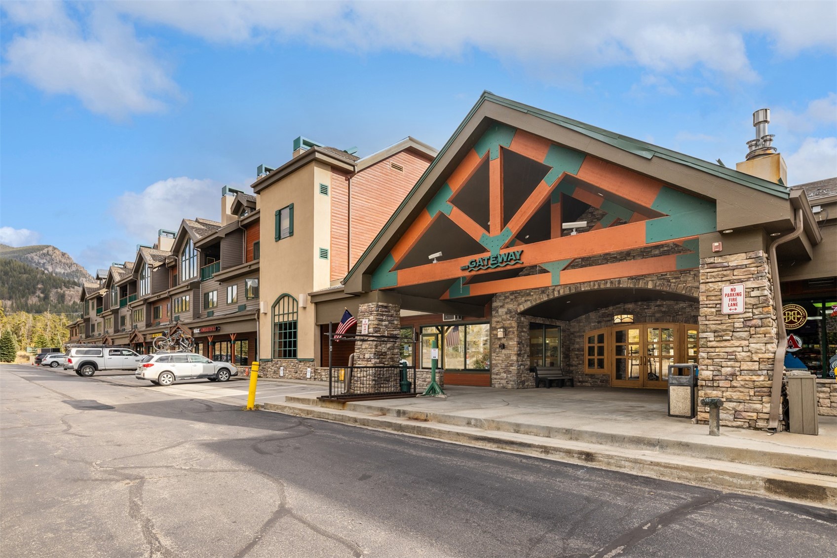 Gateway commercial building with a stone-and-timber entrance, storefronts, and a mountain slope behind it.