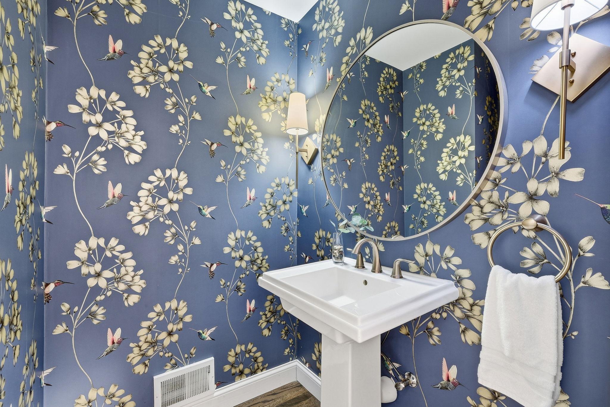 Bathroom vanity with a round mirror and blue hummingbird-and-floral wallpaper.