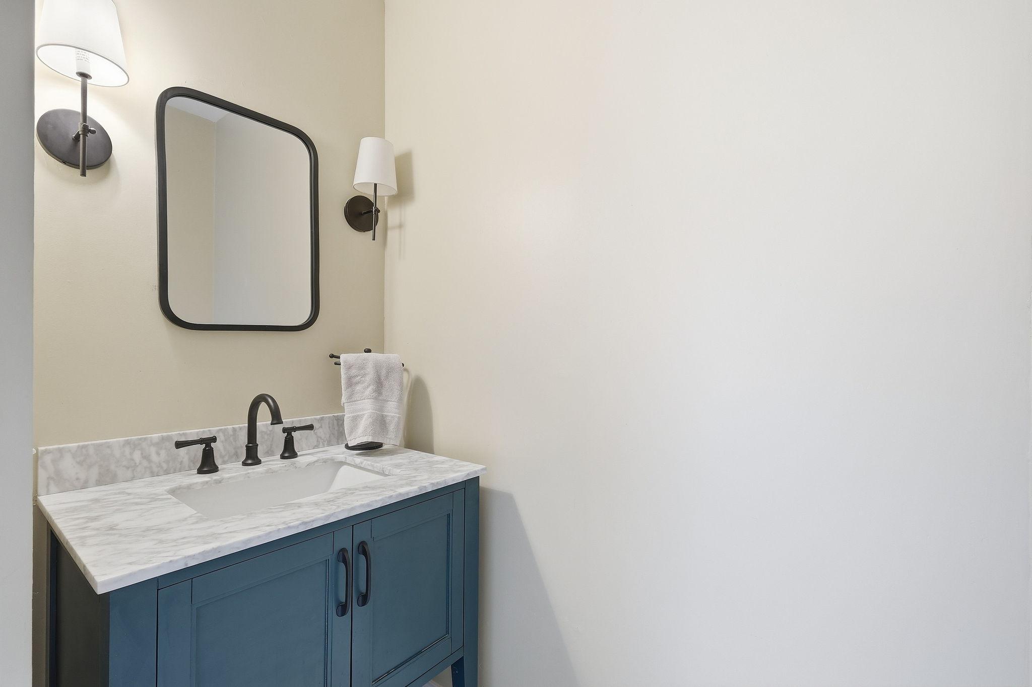Bathroom vanity with a blue cabinet, marble countertop, black fixtures, and dark-framed mirror.