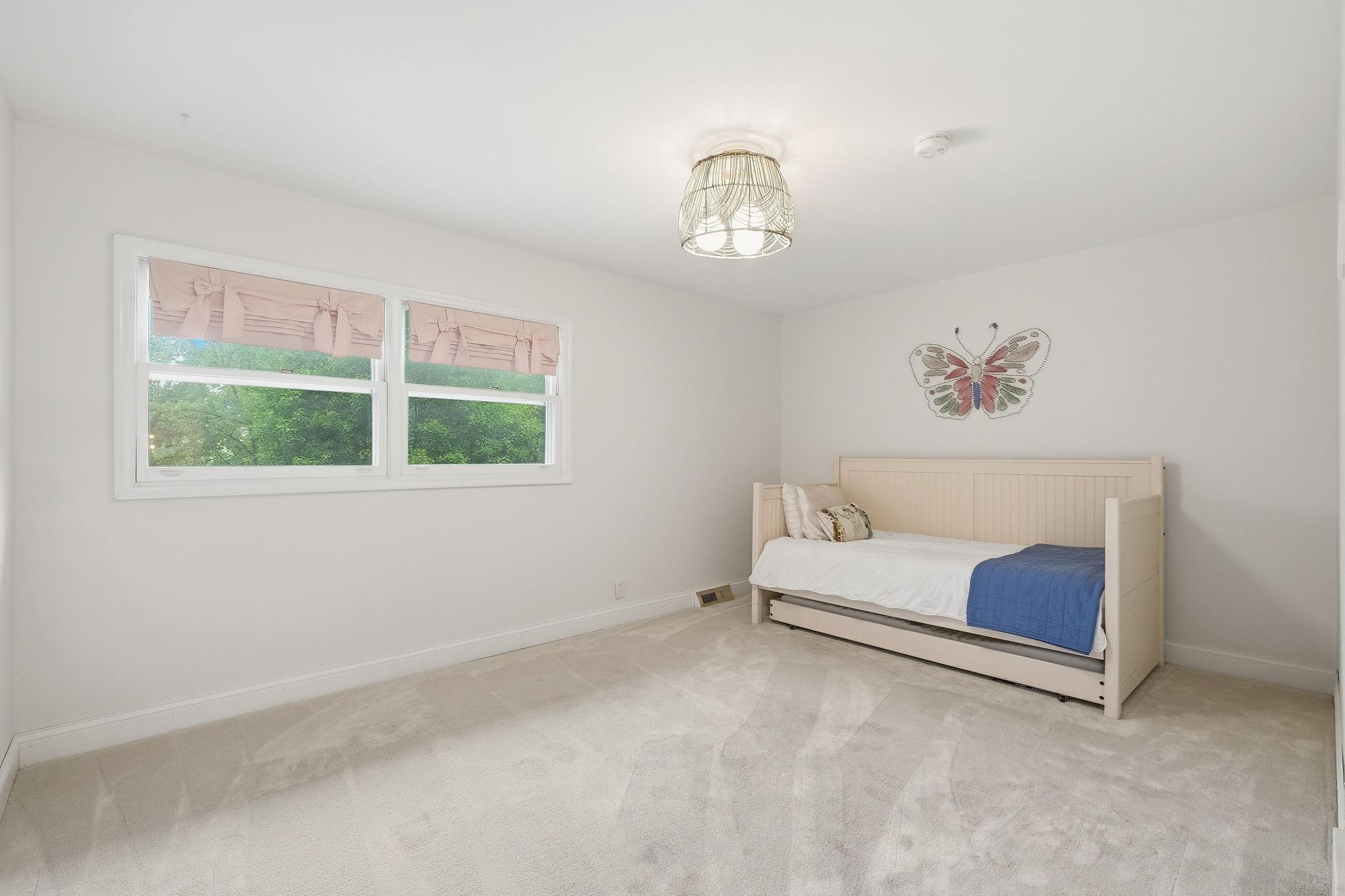 Bright bedroom with a cream daybed, blue throw, pink window shades, and butterfly wall decor.