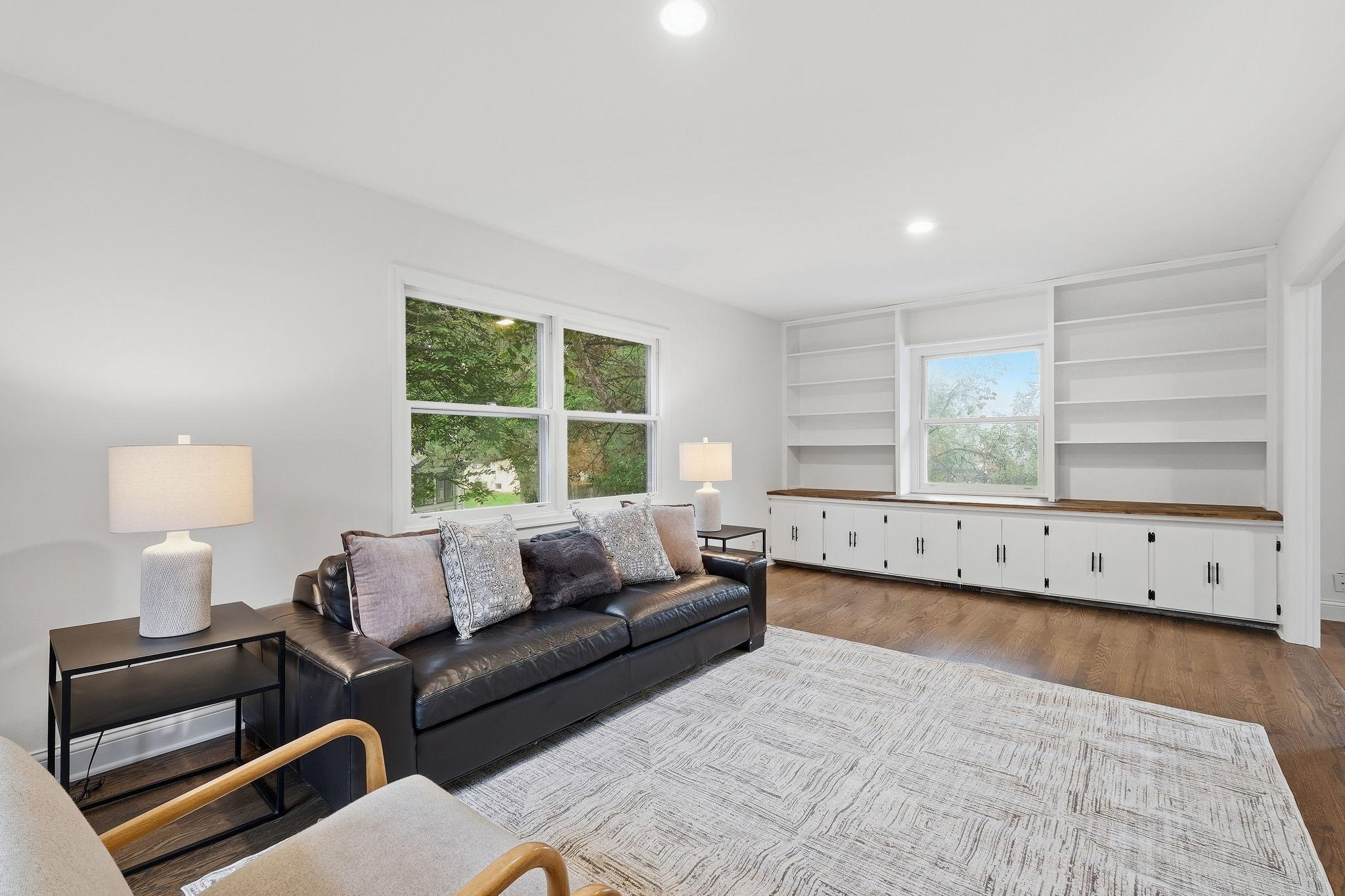 Living room with built-in shelving, large windows, and a black leather sofa.