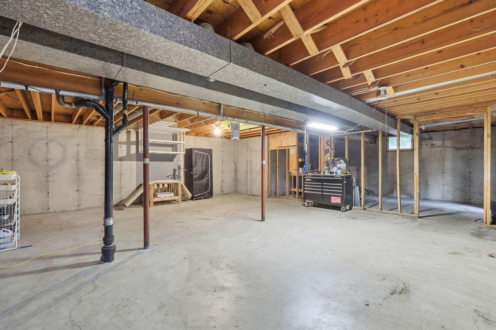 Unfinished basement with exposed ceiling joists, concrete floors, and a framed workshop area.