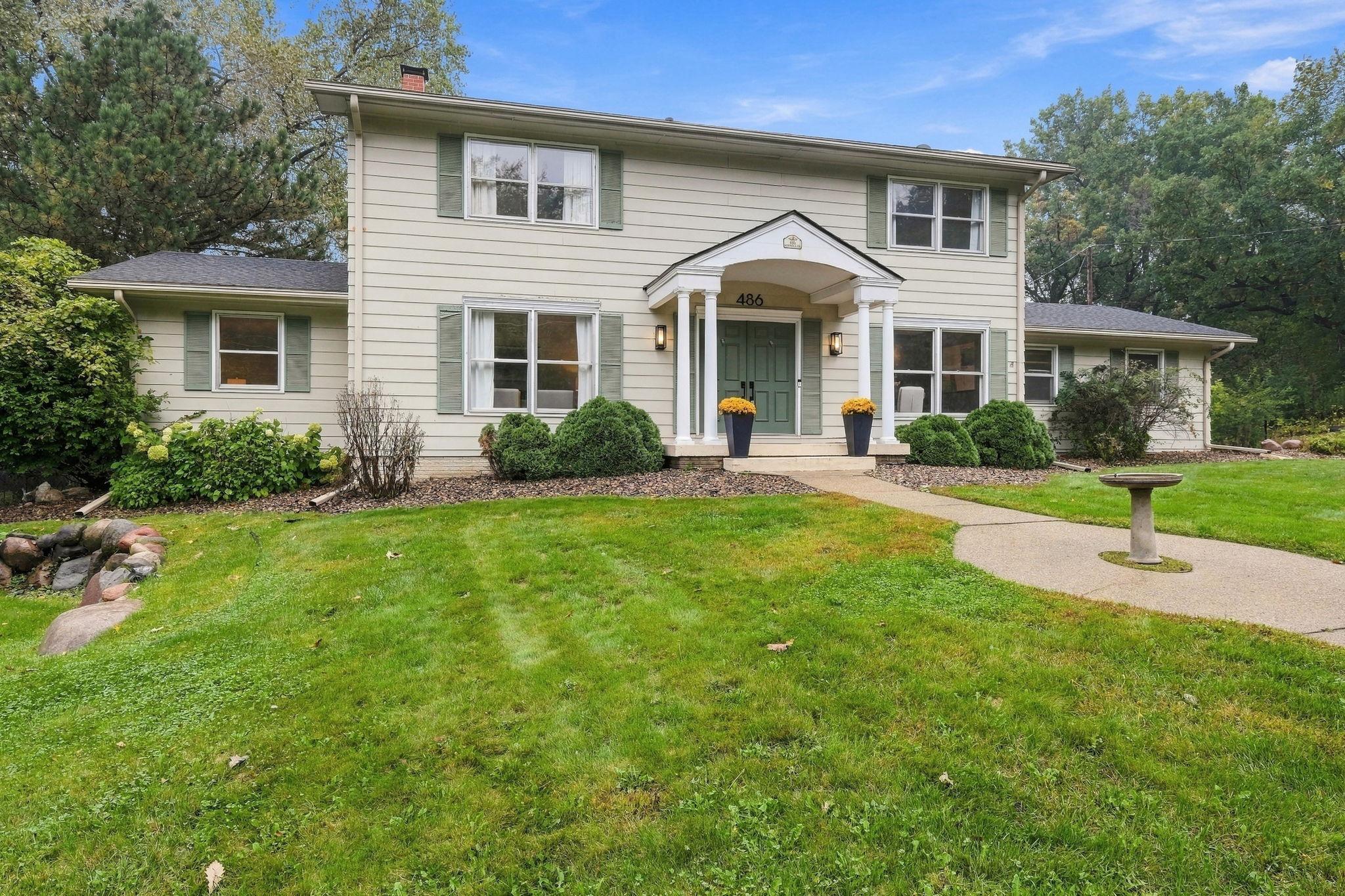 Two-story cream house with a columned entry, green shutters, and landscaped front lawn.