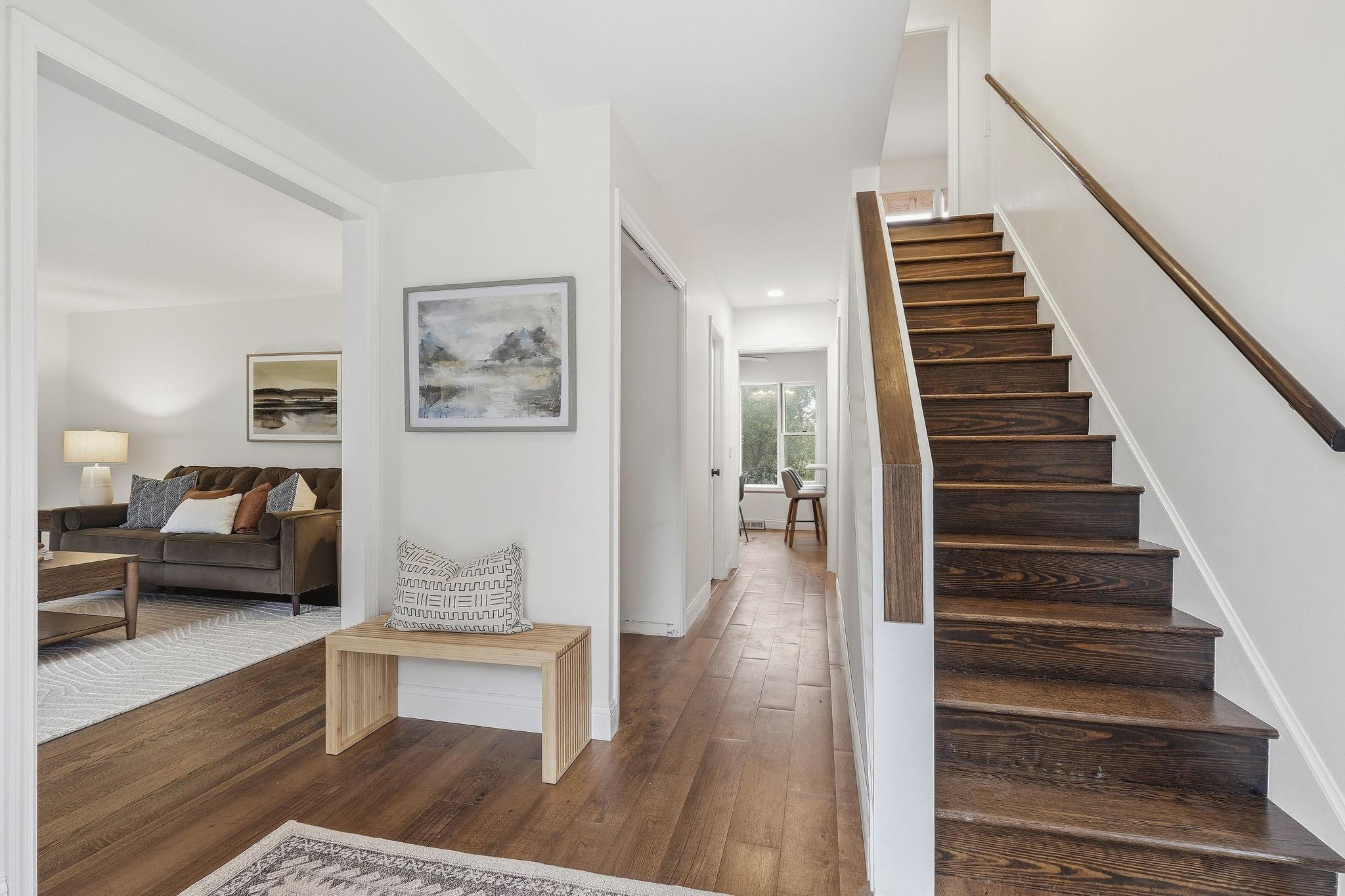Bright entry with dark wood staircase, long hallway, and adjoining furnished living room.