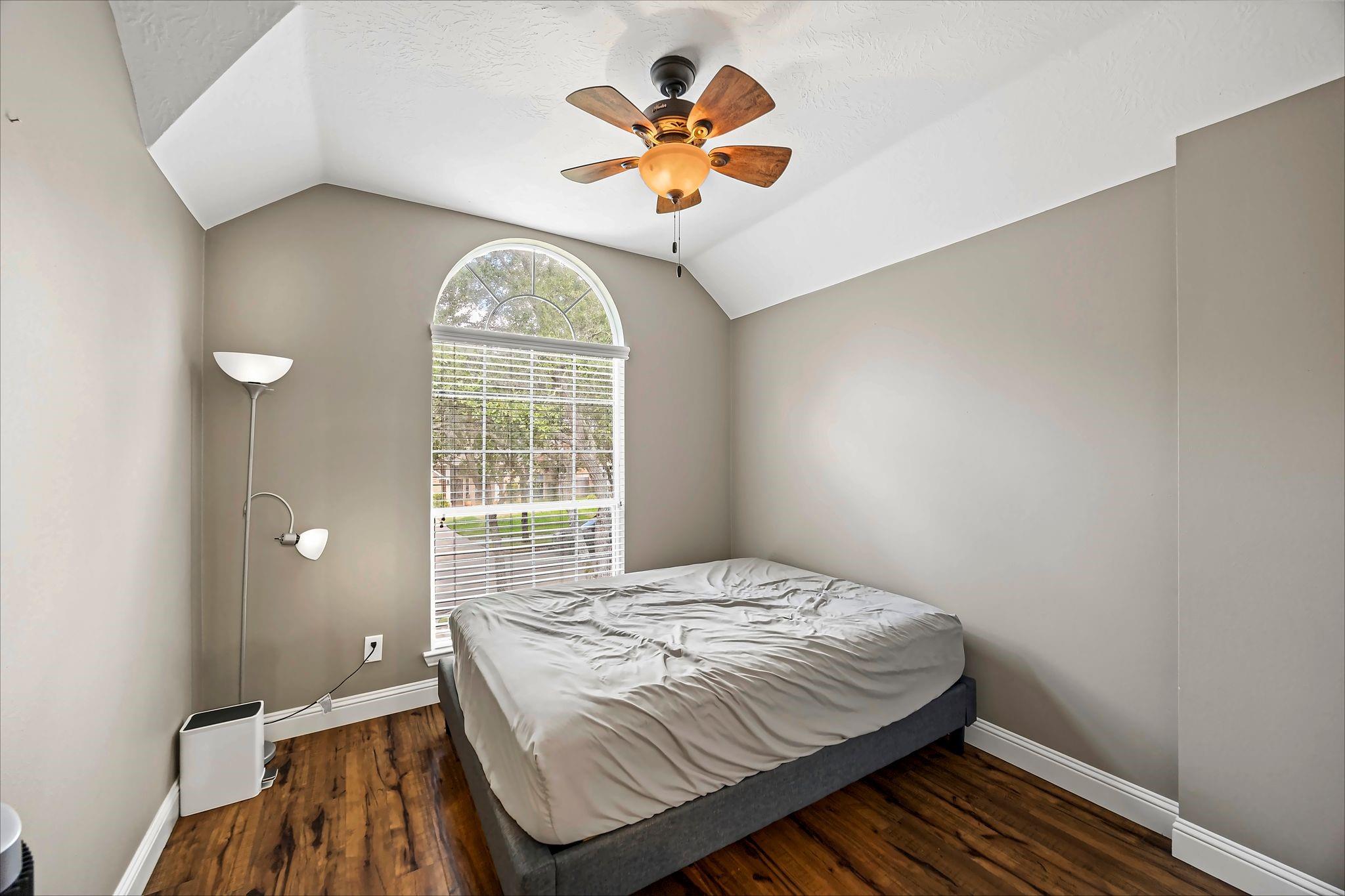 Bedroom with a vaulted ceiling, arched window, wood flooring, and ceiling fan.