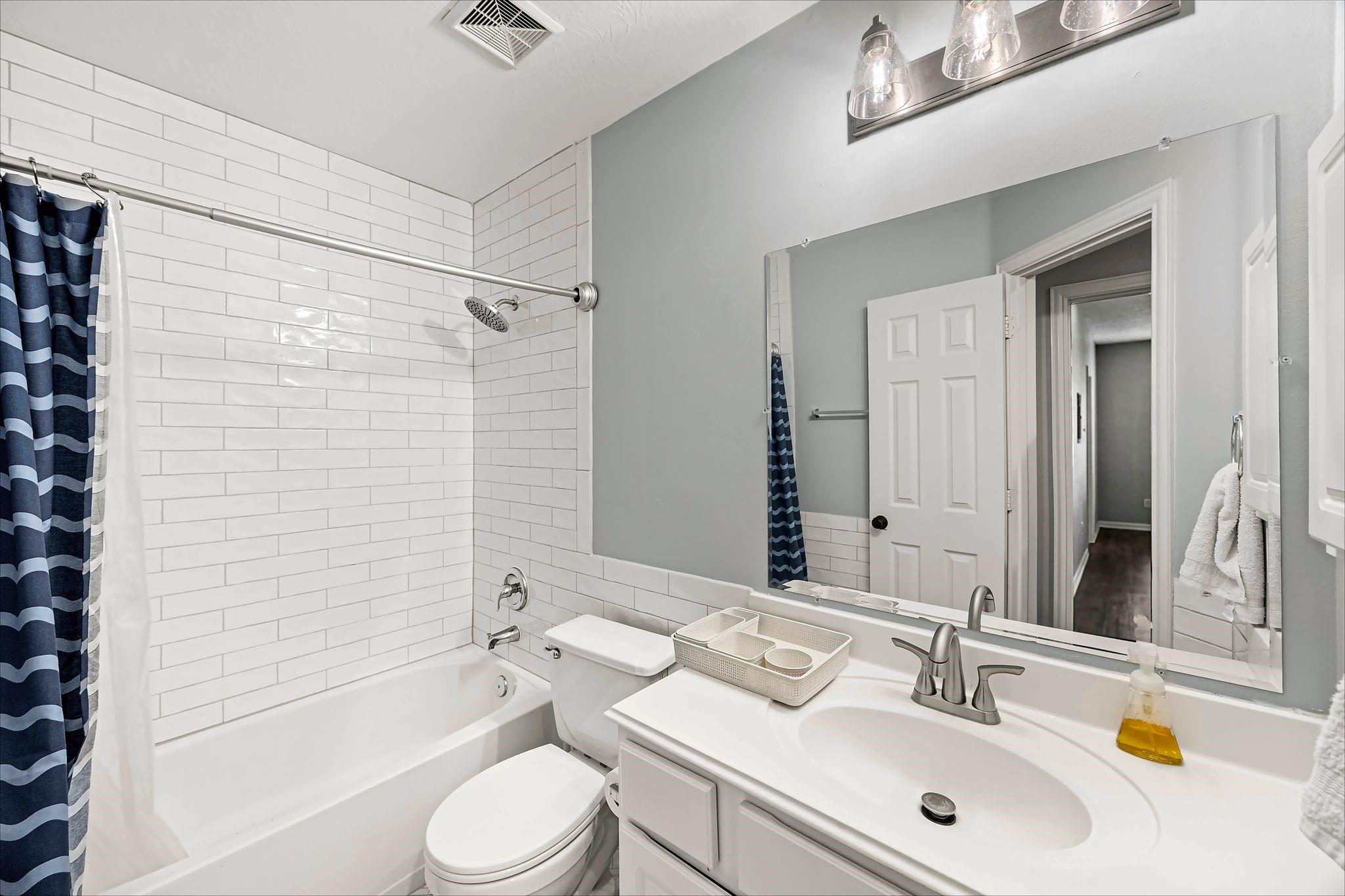 Bathroom with a white subway-tile tub and shower, navy striped curtain, and white vanity.