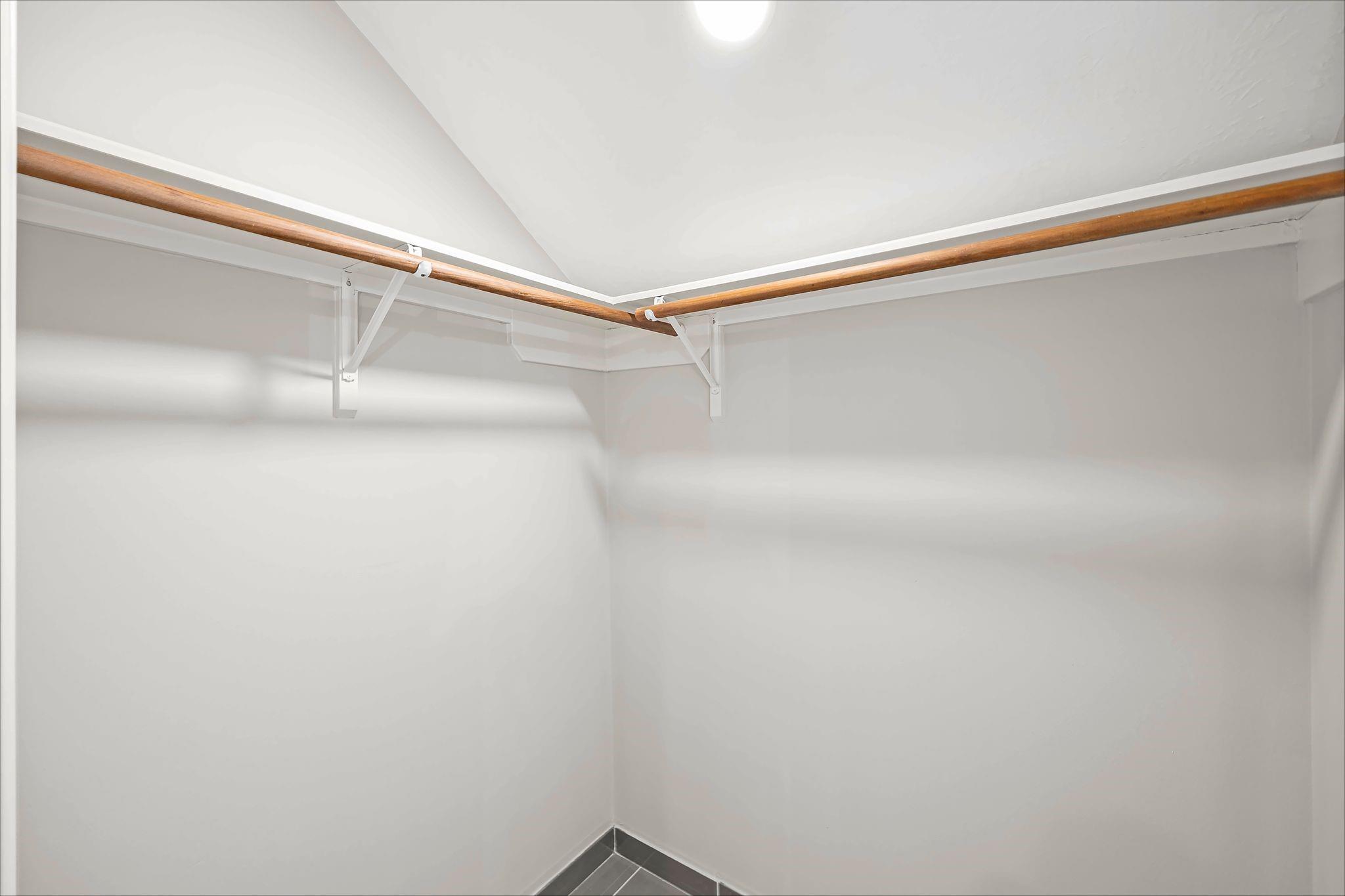 Empty walk-in closet with wooden hanging rods and dark gray tile flooring.
