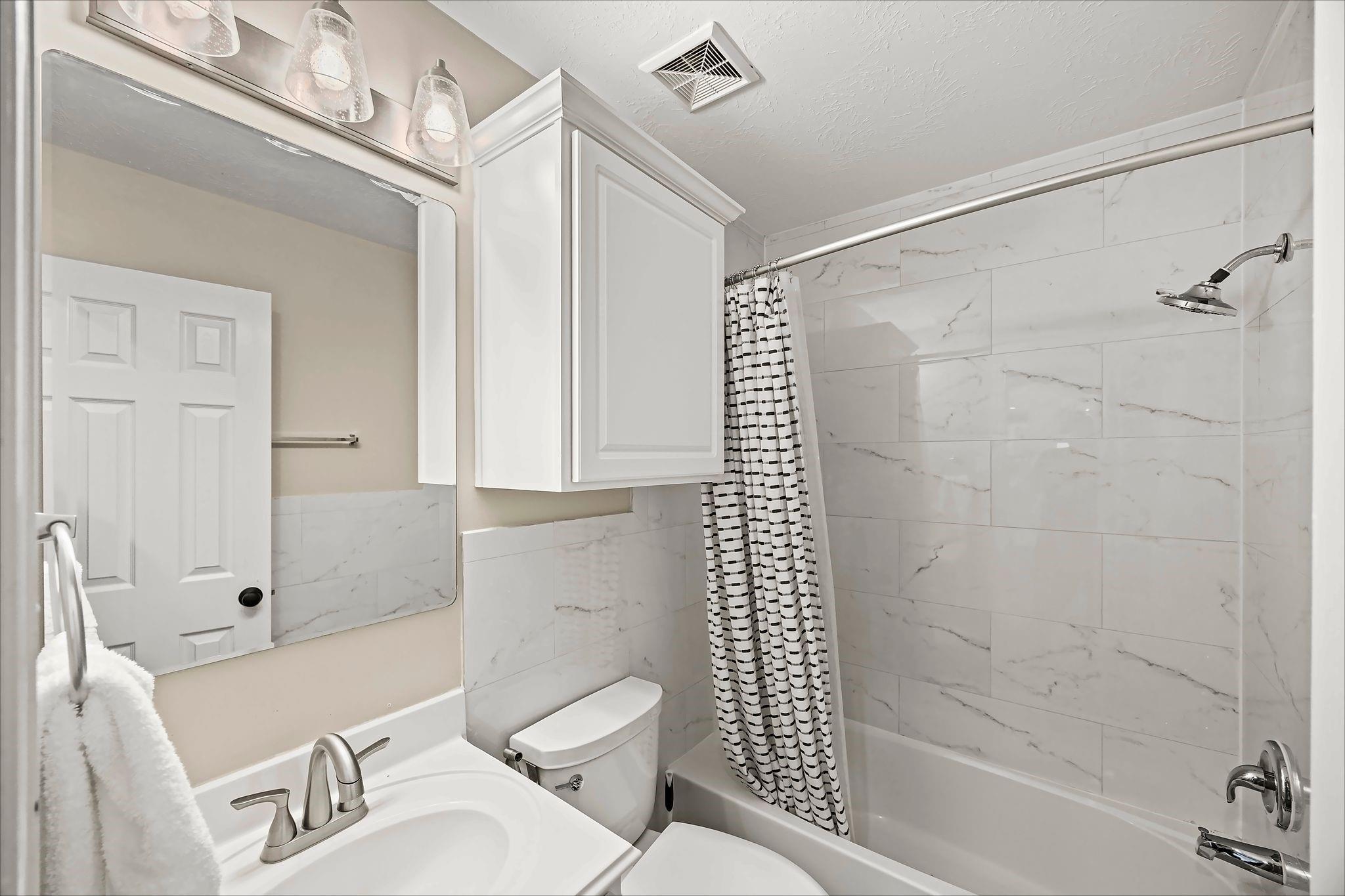 Bathroom with marble-look tub surround, white vanity, and black-and-white striped shower curtain.