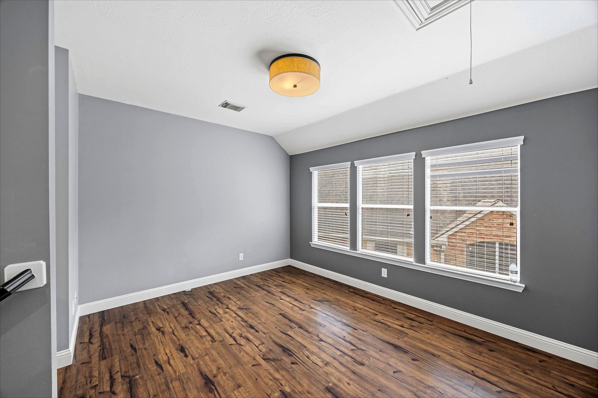 Empty room with hardwood floors, gray walls, and three windows with blinds.