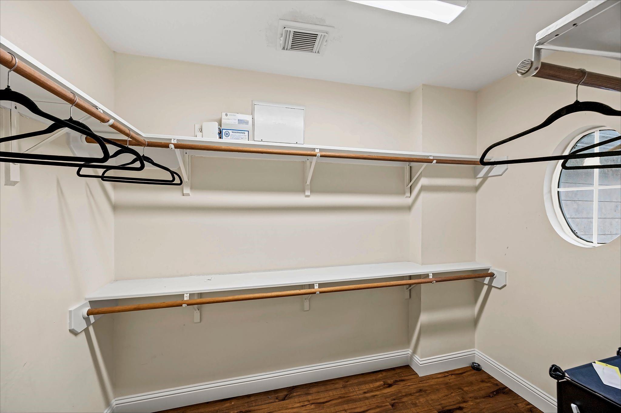 Walk-in closet with wooden hanging rods, black hangers, and a round window.