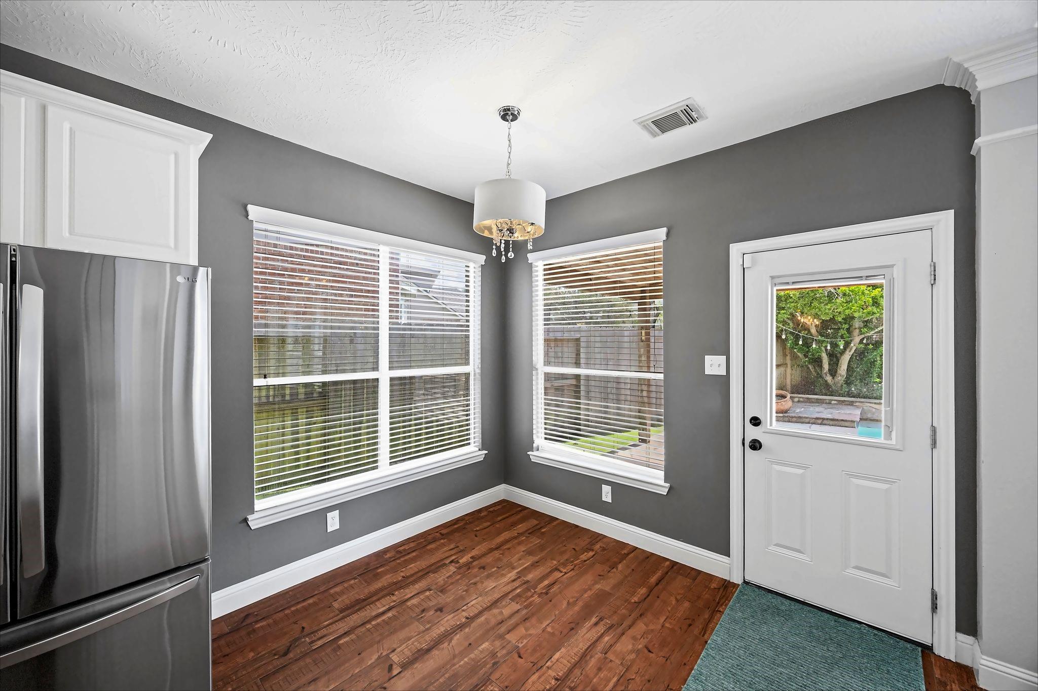 Kitchen nook with wood flooring, stainless steel refrigerator, two windows, and a glass-paneled exterior door.