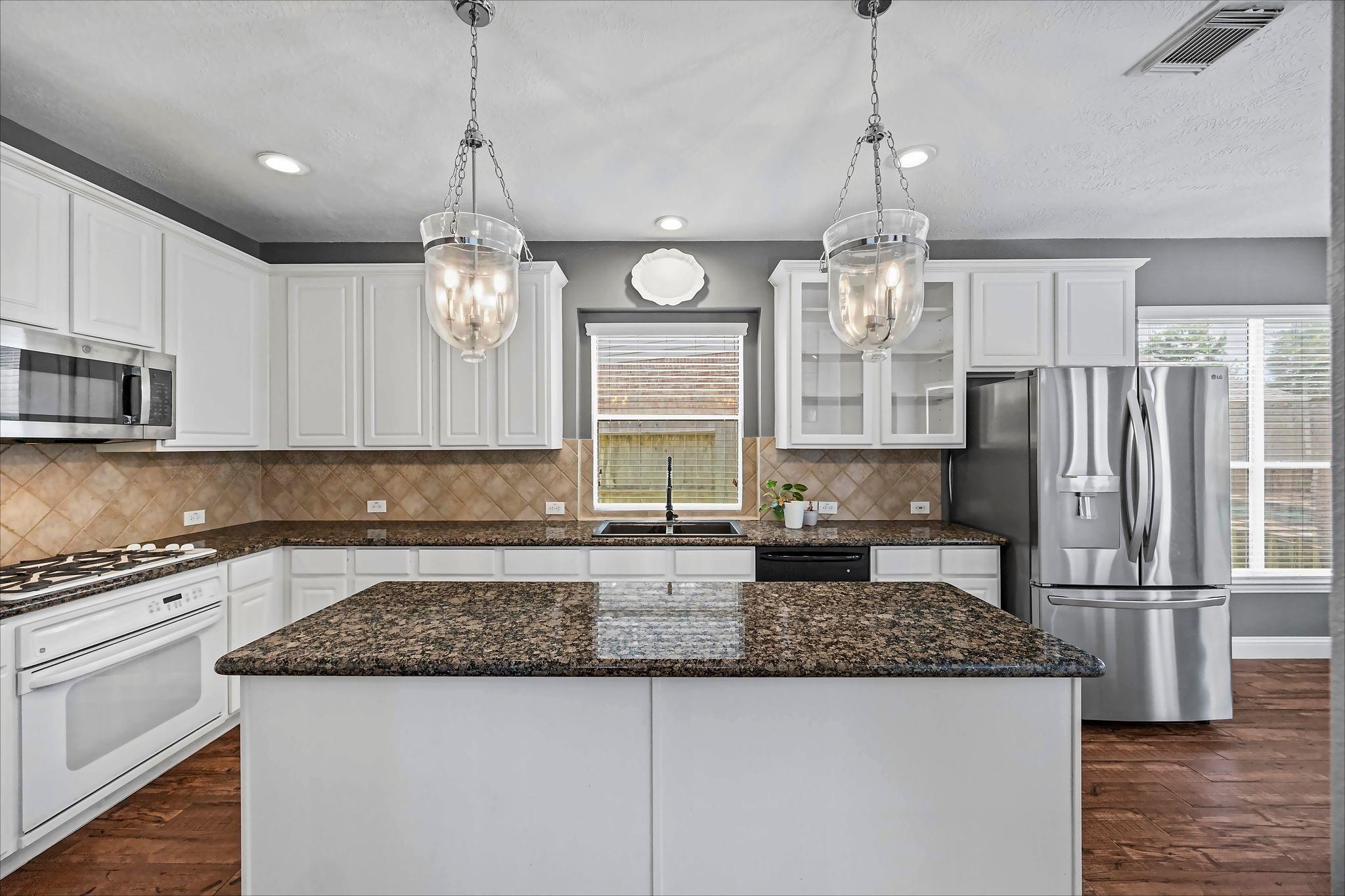 Kitchen with a large granite island, white cabinetry, and stainless steel appliances.