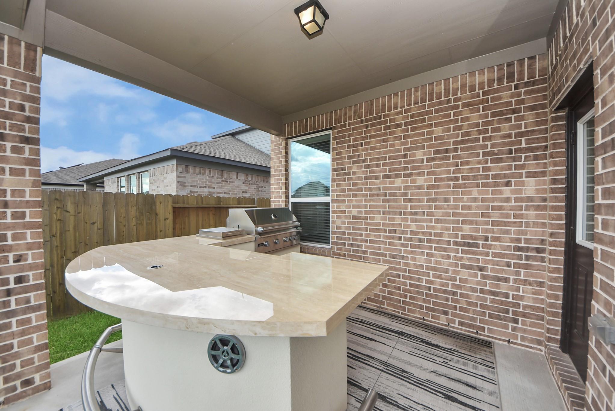 Covered brick patio with a built-in grill and large stone outdoor counter.