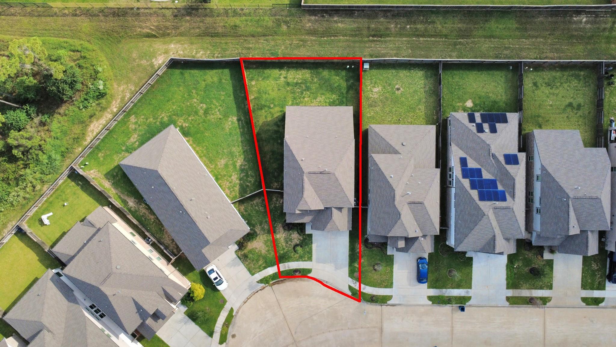 Aerial view of a home and fenced lot outlined in red, with a driveway and neighboring houses.
